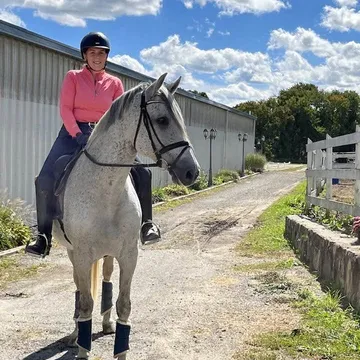 Briana “Bree” Dolbec, barn manager, riding a dappled grey horse