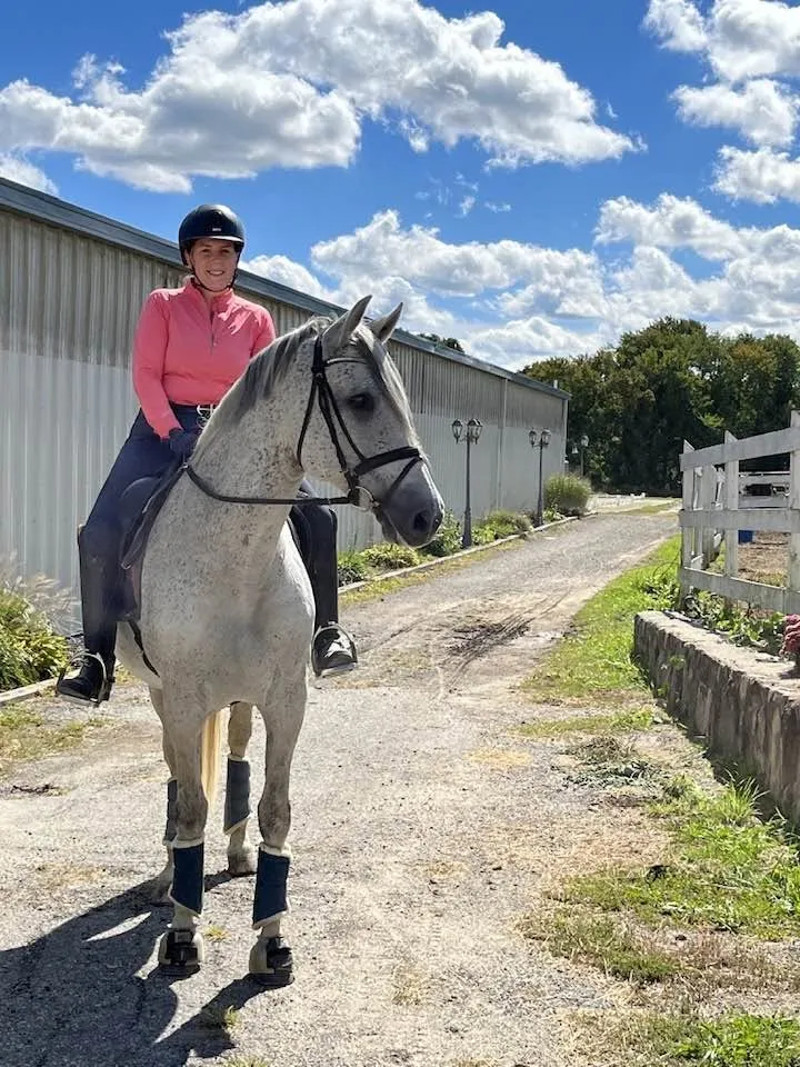 Bree Dolbec riding a dappled grey horse in a pink top under a blue sky