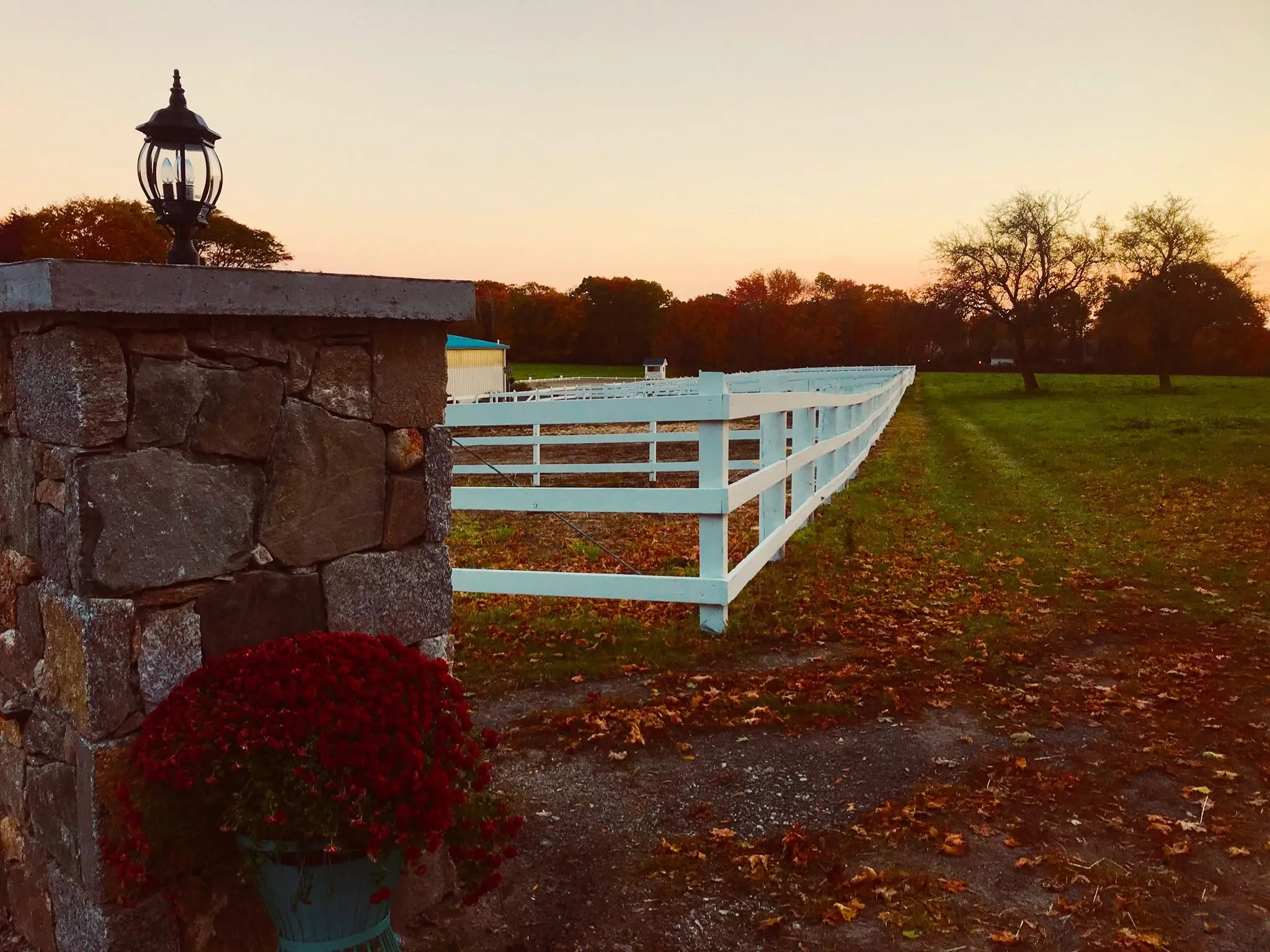 A stone pillar with a lantern and white fence at the entrance to Lepore Farm on an autumn evening