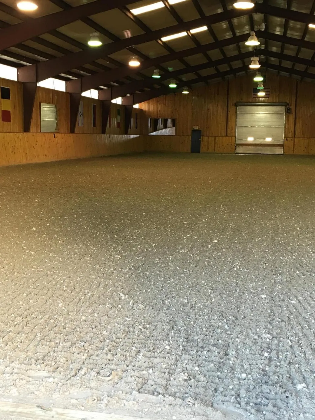 The indoor arena at Avastar with dressage flags on the wall and freshly leveled GGT footing