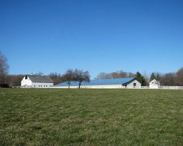A distant view of the white barn and indoor arena at Lepore Farm across a green field